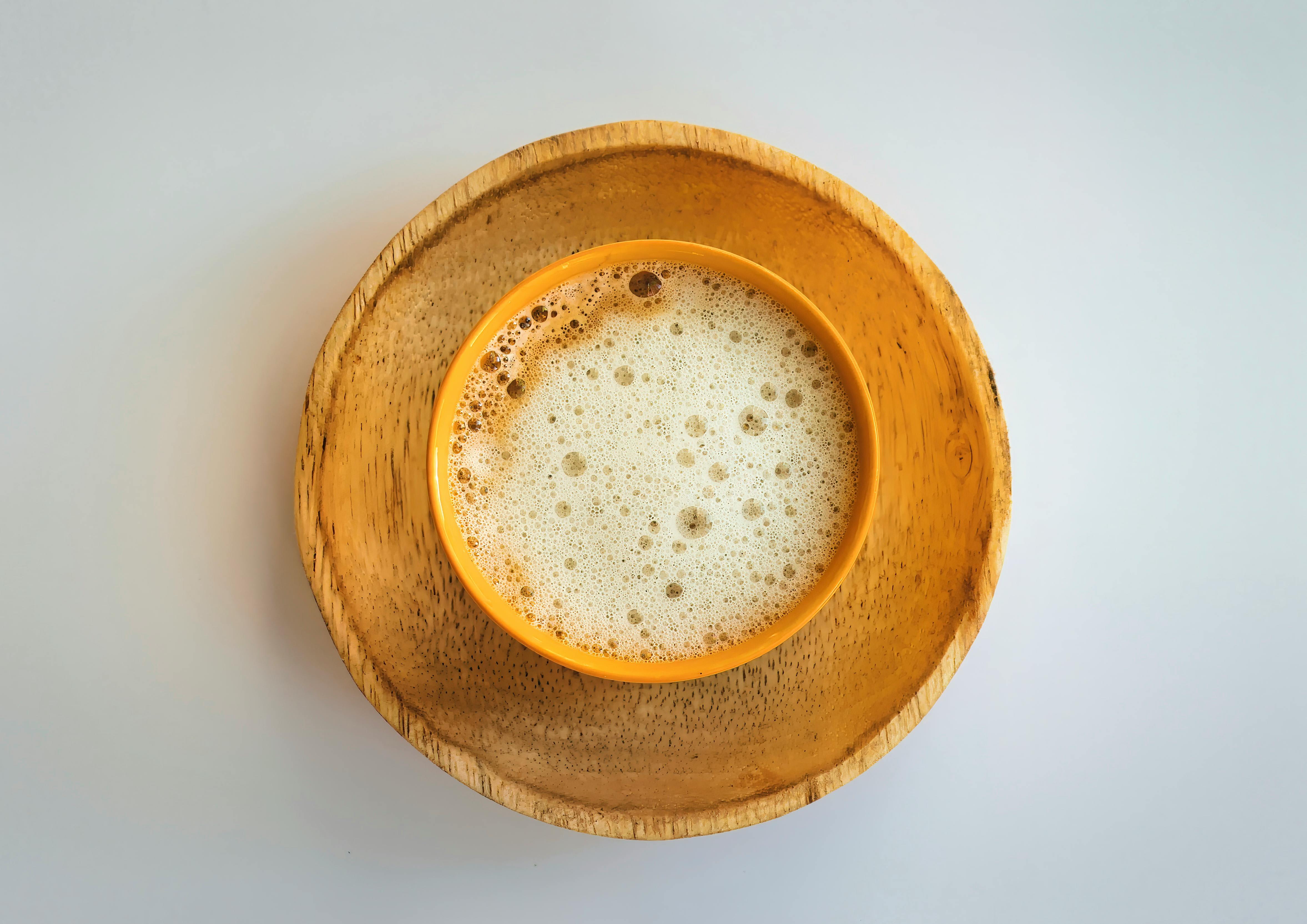 Top view of a foamy coffee cup on a wooden saucer. Minimalist aesthetic.